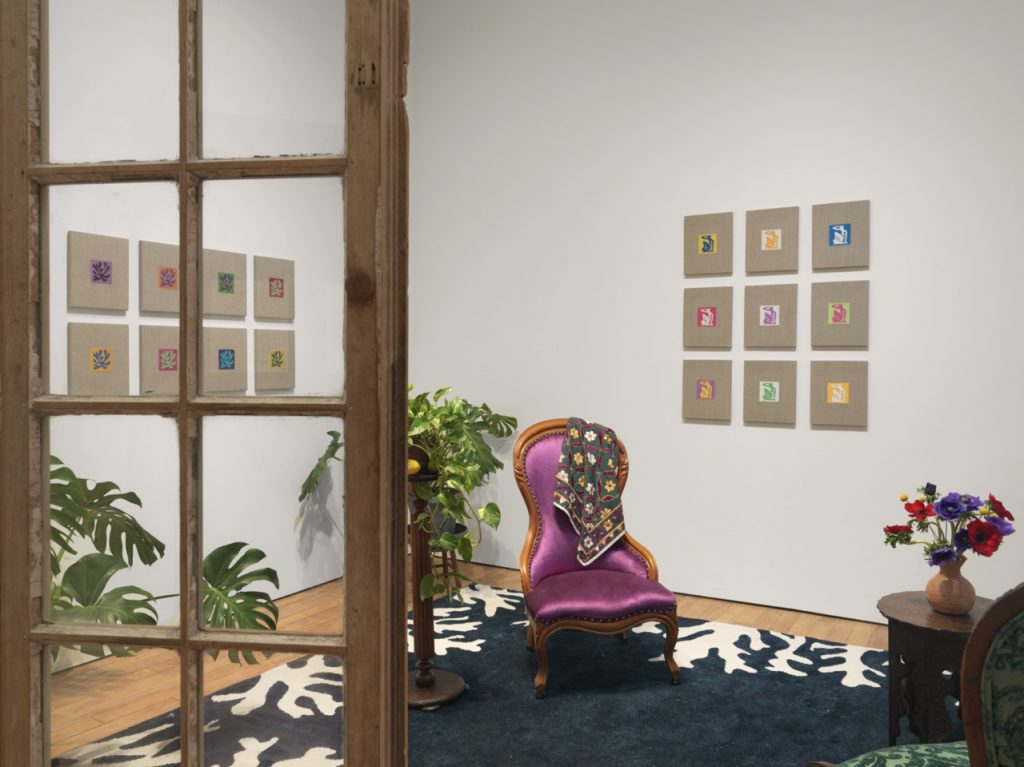 Elaine Reichek, Un petit salon après Matisse, 2022. Installation view from MATERIAL GIRL, Marinaro, New York, 2022. With (left to right): Swatches, Matisse Leaves 1–9, 2006 (8 units), and Swatches, Matisse 1–9, 2007. Installation with carpet, vintage Victorian parlor chairs, tambour table, ceramic vase, plant stand, monstera deliciosa and pothos plants, limes and lemons, hinged window sash units, and digital embroideries on linen. Dimensions variable. Photograph by Matt Grubb. Courtesy the artist, and Marinaro, New York.